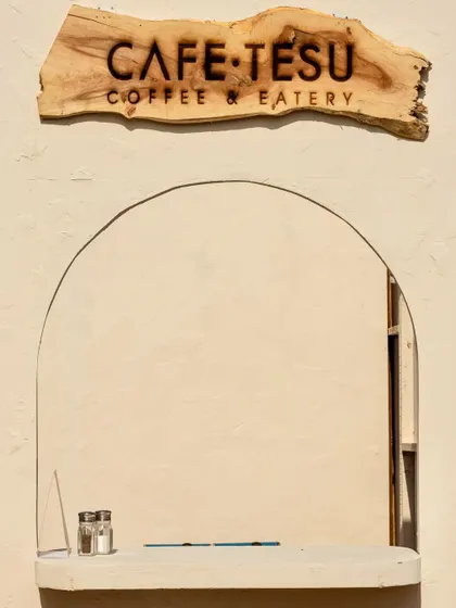 The service window of the Cafe Tesu pop-up, featuring a custom-carved wooden sign. We used simple, clean lines and an arched window to create a welcoming and minimalist aesthetic.