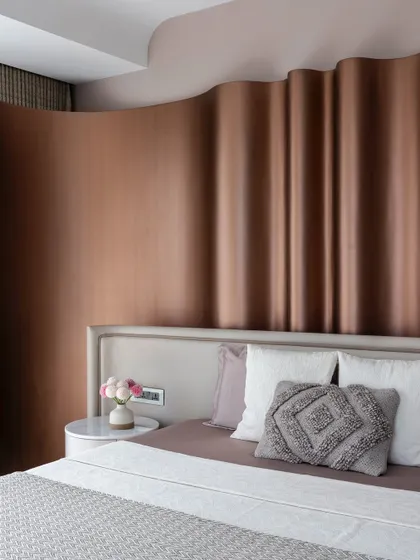 A close-up of the master bedroom in 'The House of Arcs', showing the subtle contrast of textures between the metallic headboard, soft pillows, and smooth bedside table.