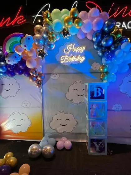A dreamy cloud and rainbow theme for a first birthday. The setup includes cloud-themed backdrops, a colorful balloon arch, and a light-up number '1'.