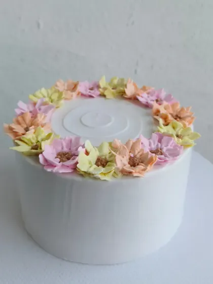 A clean white cake with a beautiful wreath of pastel-colored buttercream flowers.