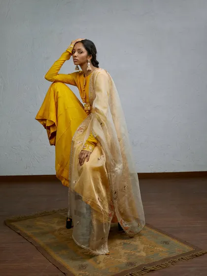 A dramatic and artistic pose for an Indian wear brand. The vibrant yellow and the flowing organza dupatta create a sculptural and visually stunning image.
