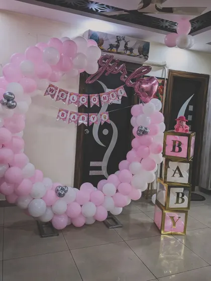 This welcome home setup for a baby girl features a full balloon ring in pink and white. The design is complemented by "It's a Girl" foil balloons and decorative "BABY" blocks for a complete look.