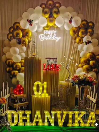 A classic first birthday decoration for Dhanvika. The gold and white balloon arch, combined with elegant props and lighting, creates a timeless and beautiful setting.