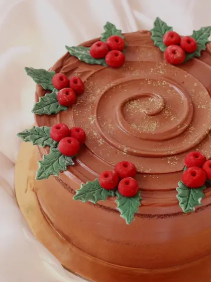 A festive chocolate yule log cake. The chocolate buttercream is textured to look like bark and decorated with holly leaves and berries for a classic Christmas dessert.