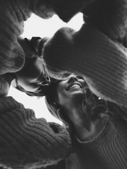 A creative, low-angle black and white shot looking up at two people in sweaters, smiling down at the camera. This playful composition captures a moment of shared joy and connection.