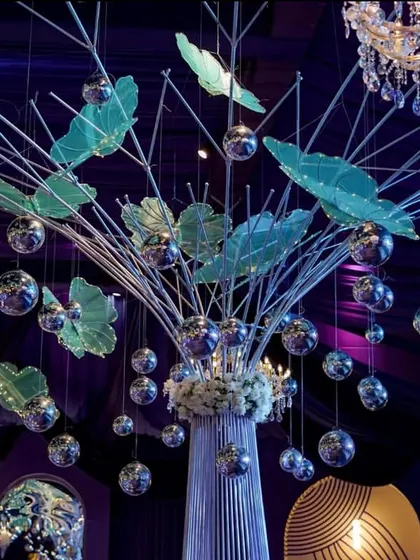 A unique centerpiece featuring abstract branches, suspended silver disco balls, and translucent green leaves that resemble butterflies. This artistic installation adds a modern, whimsical touch.