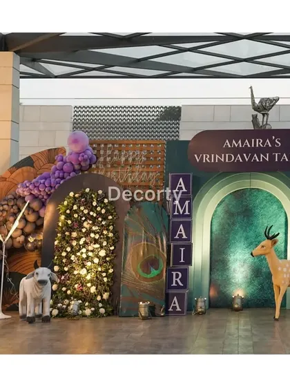 A wide view of the 'Vrindavan Tales' themed decor, showcasing a mix of floral walls, animal props like a deer and calf, and personalized name blocks for a truly immersive experience.