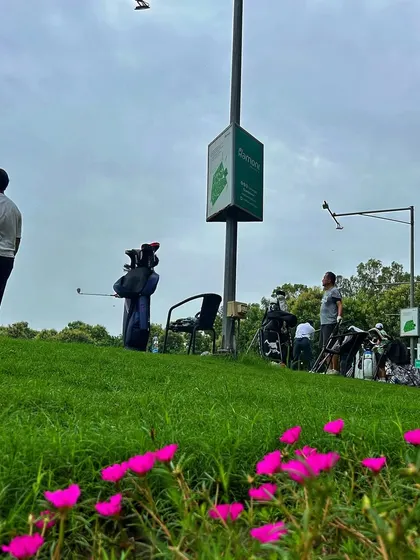 A unique low-angle shot of a golfer on the range, with beautiful pink flowers in the foreground.