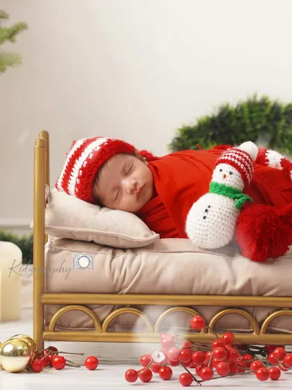 A festive Christmas-themed newborn photoshoot. The baby is dressed as a tiny Santa, sleeping soundly in a miniature bed surrounded by holiday decorations. It's a perfect way to celebrate a winter baby.