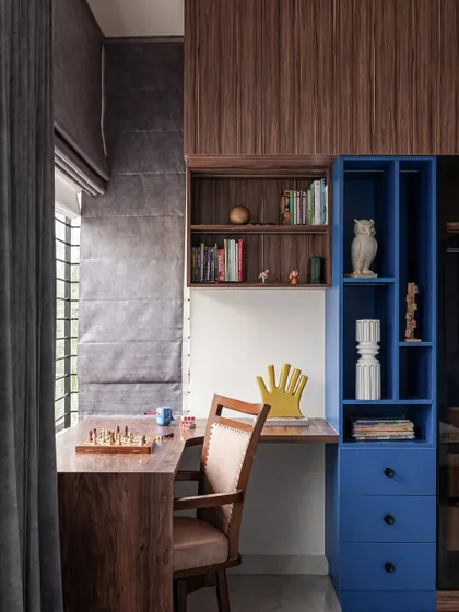 The study desk is positioned by the window to take advantage of natural light. The blue shelving unit adds a pop of color and provides organized storage for books and study materials.