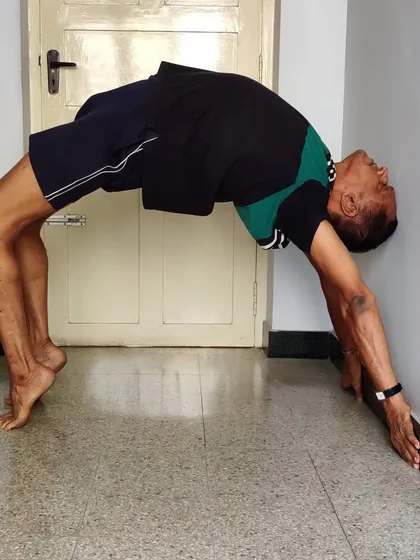Chakrasana (Wheel Pose) or Urdhva Dhanurasana, performed against a wall. The wall provides support to walk the hands down, building strength and confidence for the full backbend.