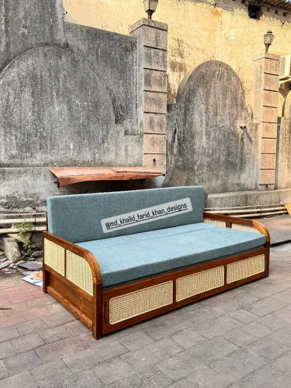 A front view of the sofa-cum-bed, showing the beautiful contrast between the wood, cane, and blue upholstery.