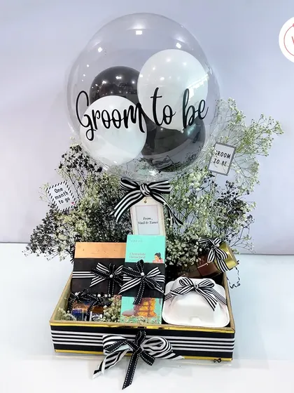 A sophisticated hamper for the groom-to-be, featuring a black and white theme with a custom balloon, gourmet cookies, and miniature bottles of spirits.