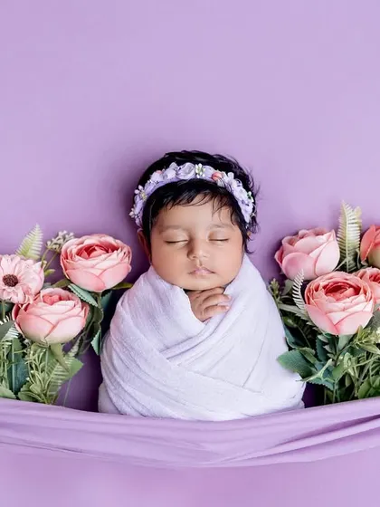 A beautiful floral arrangement for a sleeping newborn. Swaddled in white against a lavender backdrop, the baby is framed by lovely pink roses.