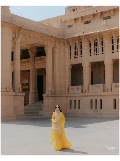 A wide shot of the bride during her haldi ceremony, capturing her against the grand architecture of Umaid Bhawan Palace.