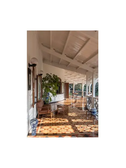 The sun-drenched verandah, with its restored geometric tile flooring and original columns, serves as a perfect transition between the interior and the lush surrounding landscape.
