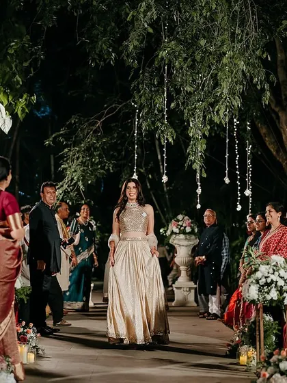 The bride's grand entrance down an aisle lined with guests, under trees adorned with hanging crystal strings.