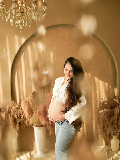 A stunning solo portrait of a mother-to-be in a lace top and jeans, basking in the warm studio light.