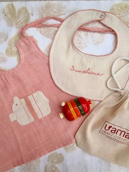 Another beautiful newborn gift set, this one featuring a naturally dyed pink top with an elephant applique. The set includes a bib and a colorful Channapatna rattle, all produced by women artisans.