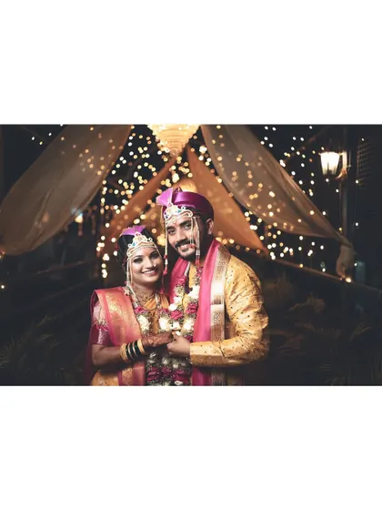 The couple holds hands, posing for a photo under a canopy of lights. This shot captures the romantic ambiance of their wedding night.
