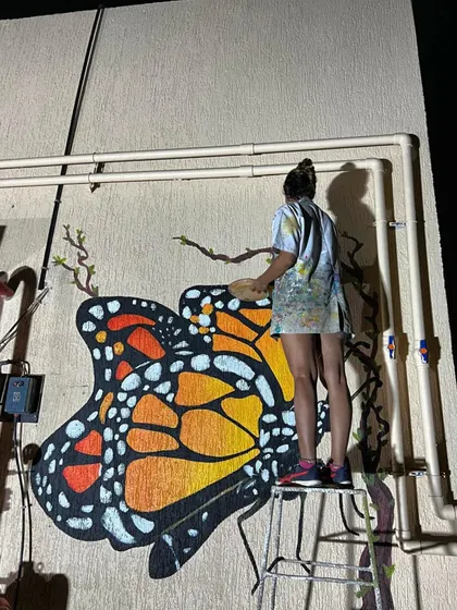 Me working on the butterfly mural at night, perched on a ladder to paint the intricate details of the wings.