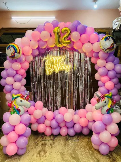 A unicorn-themed balloon arch for a 12th birthday, featuring a silver fringe backdrop, unicorn head balloons, and a neon sign.