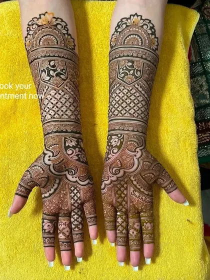 A beautiful, symmetrical bridal design with shield-like patterns on the arms and delicate work on the hands. The name 'Sukha' is written on the fingers.