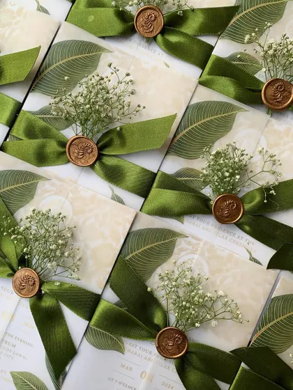 A beautiful array of engagement invitations for S&A, showcasing the consistency and craftsmanship of our work. Each invitation is wrapped in a vellum sheet with a leaf design and secured with a green satin ribbon, a custom wax seal, and a sprig of fresh baby's breath.