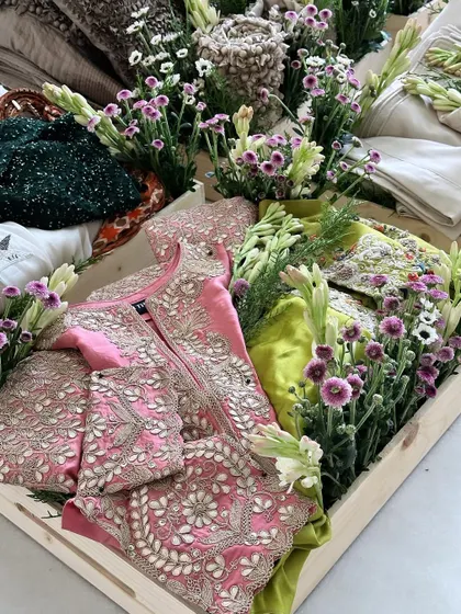 A tray filled with vibrant outfits in pink and lime green, all brought together with an arrangement of fresh tuberoses and purple daisies.