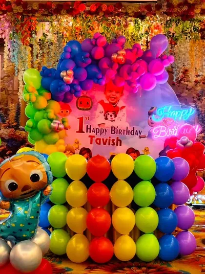 A detailed look at a Cocomelon first birthday stage. This setup includes a lit-up number "1", a neon "Happy Birthday" sign, and multiple character balloons, making it visually packed and exciting.