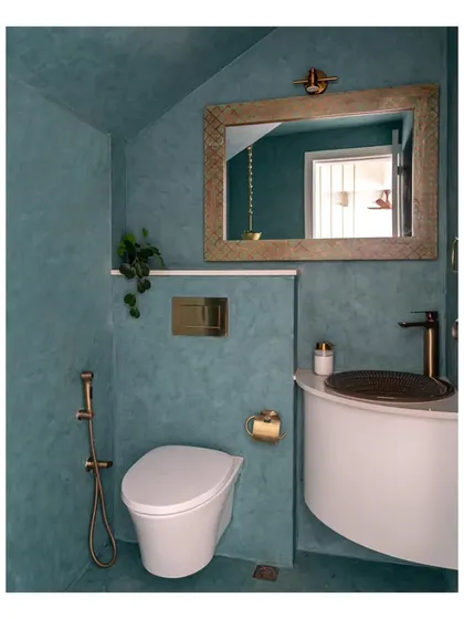 The powder room, revamped with a greenish-blue micro-topping that contrasts beautifully with antique-gold faucets. A distressed green-gold mirror adds a touch of sparkle to the compact space.
