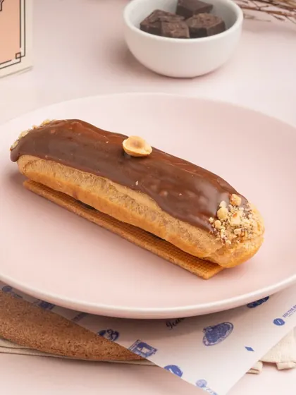 The Hazelnut Eclair, showcasing its smooth milk chocolate glaze and a single hazelnut as a garnish.