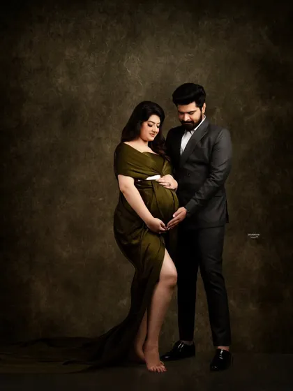 A sophisticated and intimate couple portrait against a dark, painterly backdrop. The contrast between her olive green gown and his dark suit creates a rich, elegant look.
