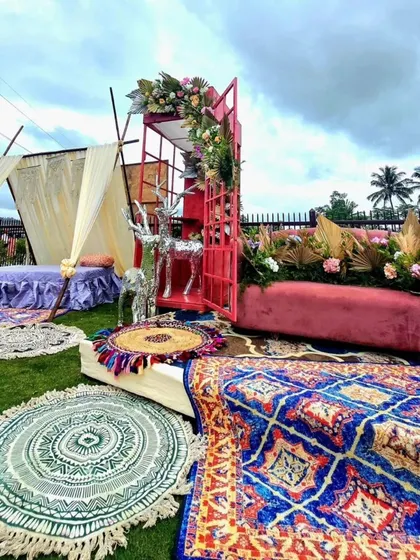 A bohemian-chic outdoor seating area. The setup includes low seating on colorful rugs, a teepee tent, and a velvet sofa, creating a relaxed and stylish vibe.