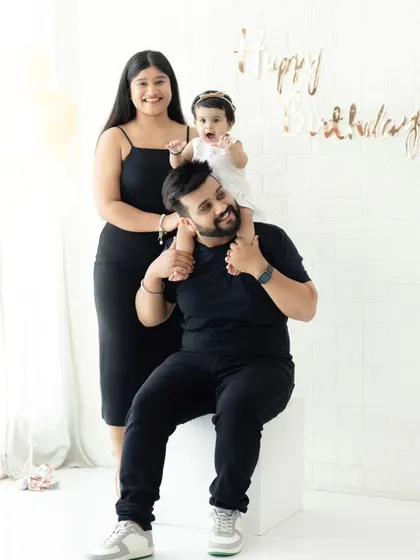 A happy family celebrating their daughter's first birthday. Having the baby on dad's shoulders adds a fun and playful element to the family portrait.