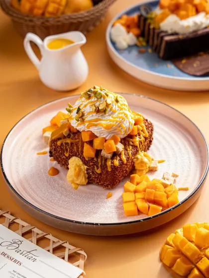 A slice of mango tres leches cake from Bastian. The close-up highlights the layers of cake, cream, and fresh mango, emphasizing its rich and moist texture.