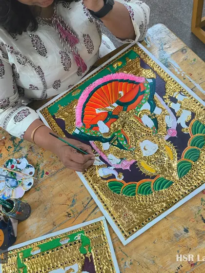 An overhead view of a student engrossed in painting a Tanjore masterpiece. The table is filled with brushes and paints, showing the hands-on nature of our workshops.