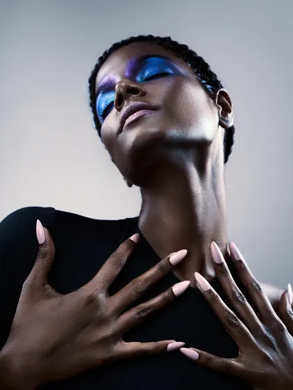 This beauty shot highlights the nails and makeup. The pose draws attention to the hands, while the lighting accentuates the metallic sheen of the eyeshadow.