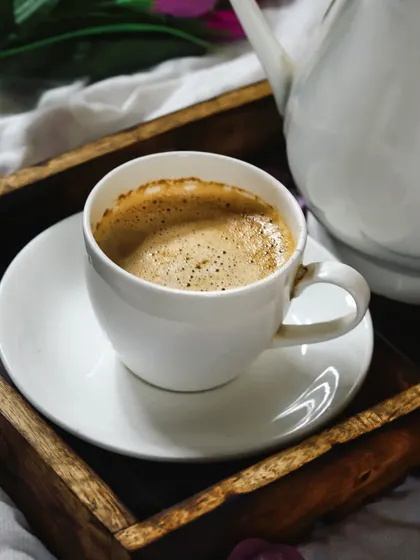 A close-up of a frothy cup of coffee on a wooden tray. The simple composition and clean white porcelain make this a timeless and classic coffee shot.