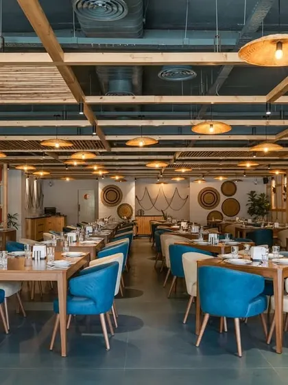 The open layout of 'Coast II Coast' allows for flexible seating arrangements. The lighting, with its woven shades, adds to the coastal ambiance while providing warm, focused light for each table.