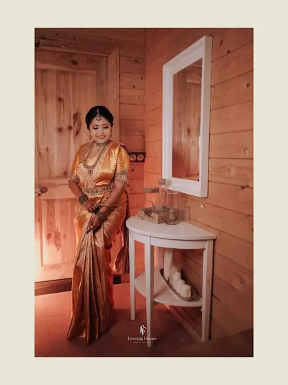A full-length shot of the bride in her golden saree, standing in a beautifully lit room.