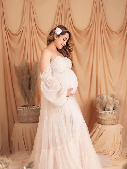 A full-length portrait in a dreamy, bohemian-style white gown with puffy sleeves, set against a neutral backdrop.