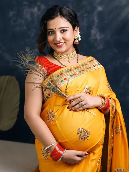 A lovely portrait of the expecting mother holding a peacock feather. Her gentle smile and traditional jewelry complete the look, making this a classic Indian maternity photograph.