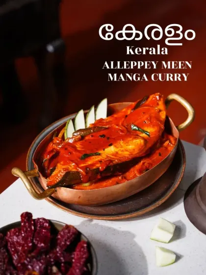 A vibrant red Alleppey Meen Manga Curry from Kerala, served in a traditional copper pot. The image, with its bold color and simple styling, speaks to the authentic and spicy flavors of the region.