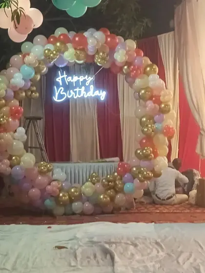 An outdoor party setup at night, featuring a large pastel-colored balloon ring with a 'Happy Birthday' neon sign. This shows how my decorations can be the centerpiece of an evening event.