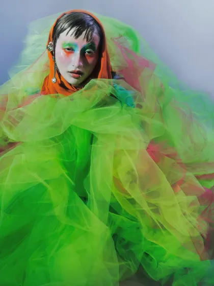 The model is enveloped in a cloud of bright green tulle, with only her face visible. This image uses color and texture to create a sense of being submerged within a vibrant, emotional substance.