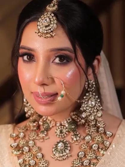 A close-up showcasing a stunning reception look. The makeup features a dramatic winged liner, shimmering glitter on the eyelids, and a glossy nude lip. The skin is kept dewy and highlighted to catch the light beautifully.