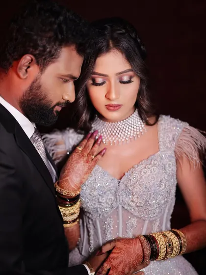 An intimate portrait of a couple dressed in modern reception attire. This shot focuses on their connection, highlighting the bride's intricate gown and henna-adorned hands against the groom's classic suit.