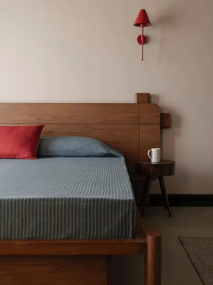 A pop of color in a bedroom at Apartment 1005, with a red wall lamp and pillow contrasting against the warm wood of the custom bed.