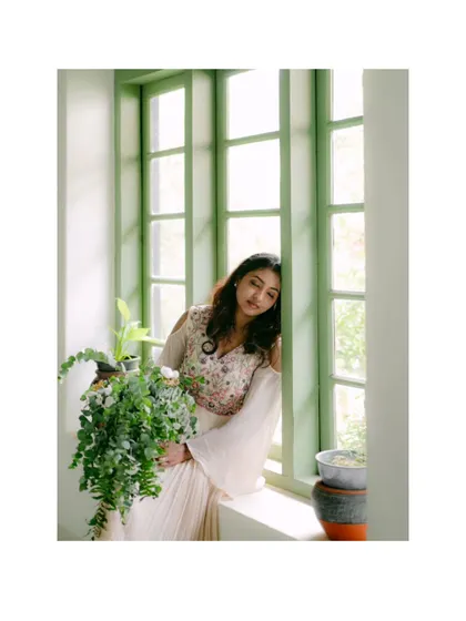 A bride leans against a green window frame, holding a plant. This artistic portrait combines natural elements with a sense of calm and serene beauty.